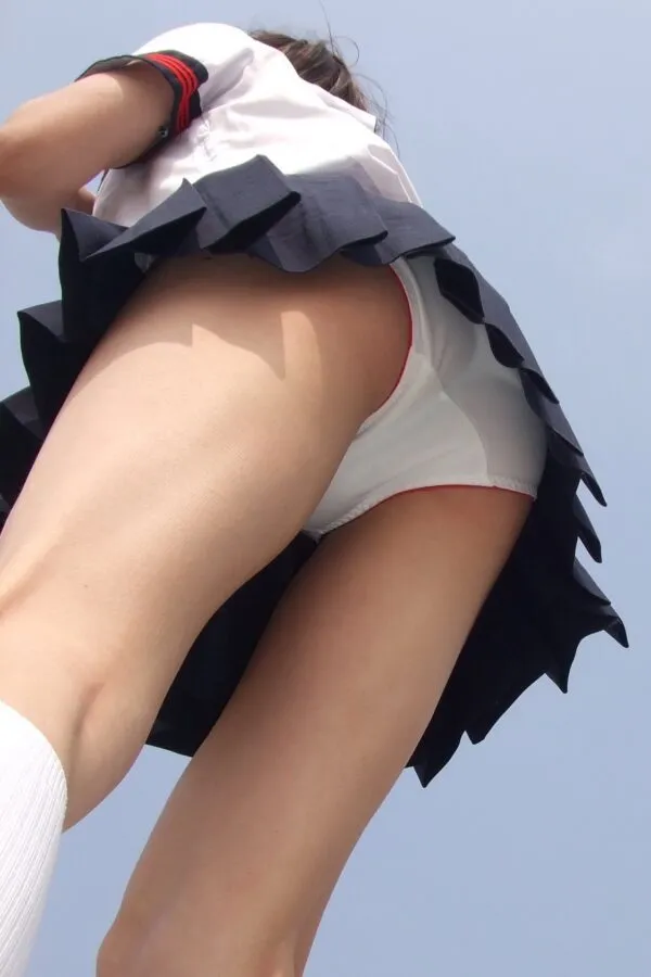 JK制服の紺色スカートを穿いた女が青空の下でローアングルから撮影され、白地に赤縁のおぱんつが見えるムチムチ尻が淫らに強調されているシーン