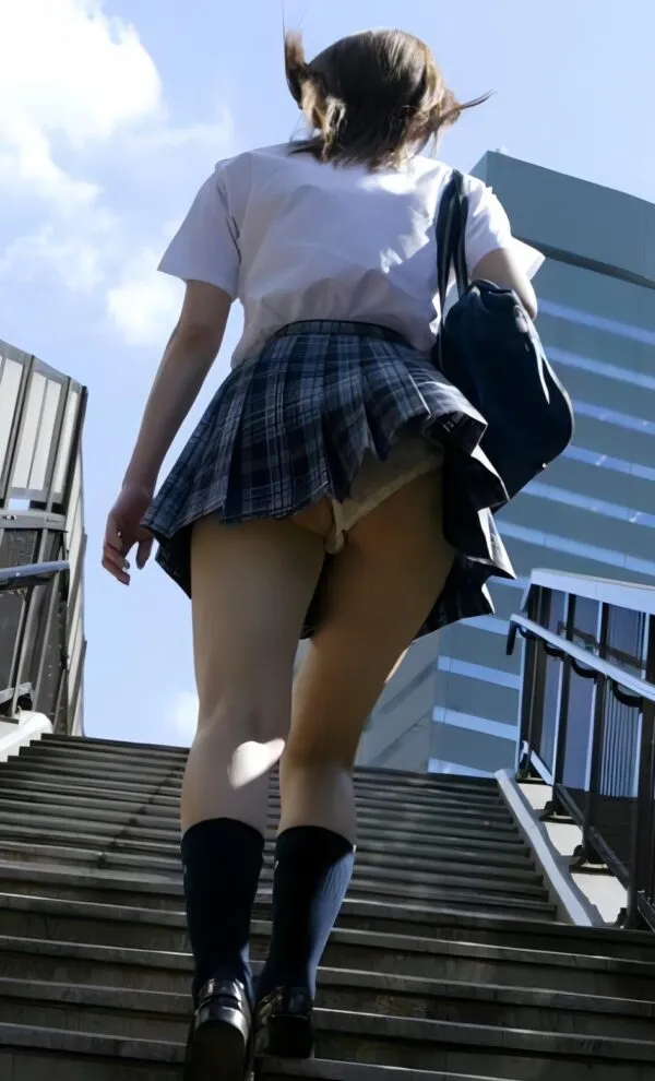 青チェック柄スカートを履いたJKが階段を上る後ろ姿で、透け感のあるベージュ色パンツからムチムチ尻が卑猥に見え、青いバッグを肩にかけた姿が青空を背景に映える。