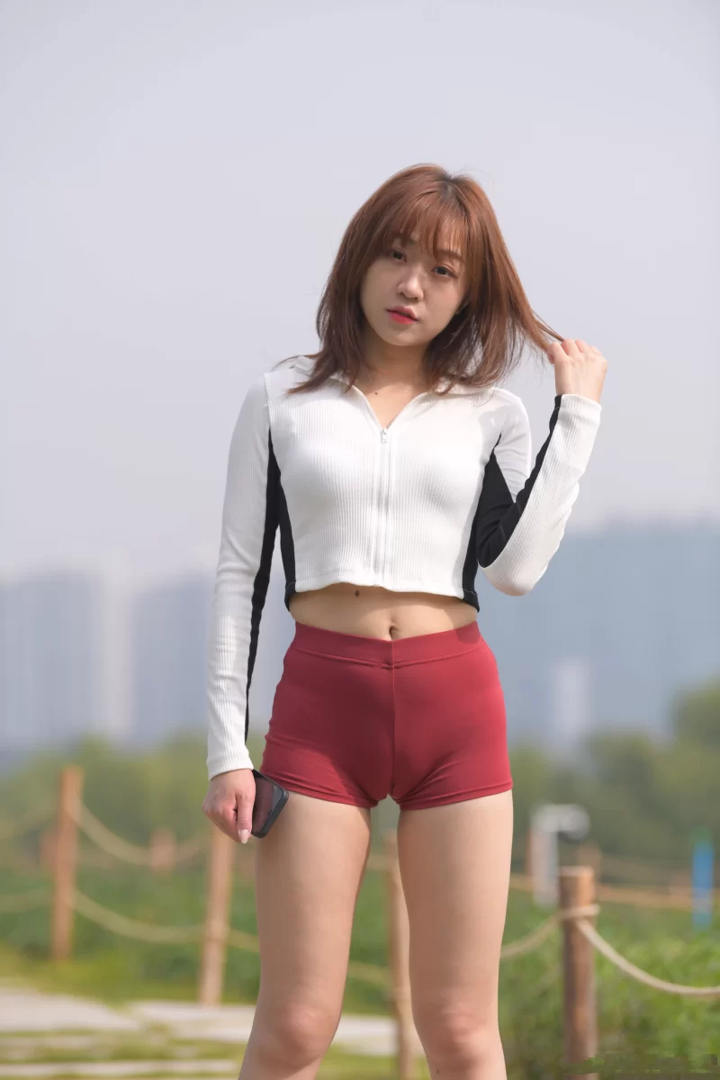 野外で立ち姿の女性が赤い競技用ショートパンツを履き、股間にマンスジが浮き出ている様子