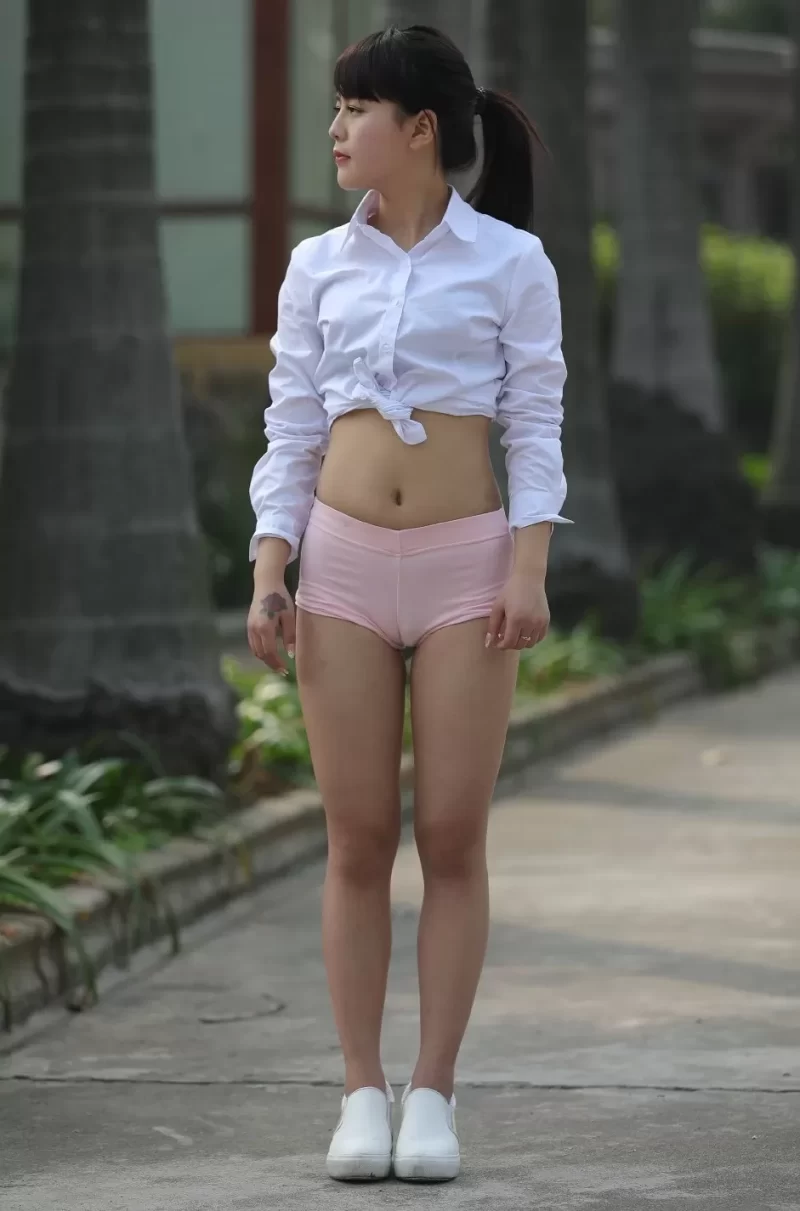 屋外で立ち姿の女性がピンクの競技用ショートパンツからマンスジが見える股間と太ももを露出している様子