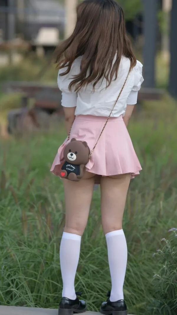 ミニスカートを履いた女が屋外の草むら近くで背を向けて立ち、ピンク色のミニスカートから淫らに露出した生尻を撮影したエロ画像。