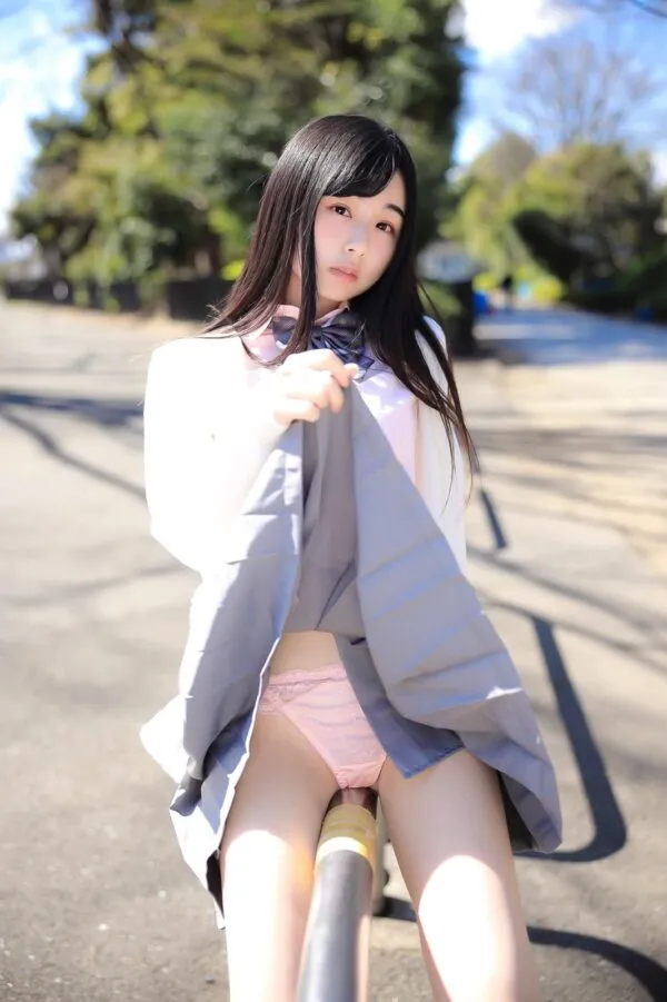 屋外で座りながら制服のグレーのスカートをめくり、ピンクのレースパンツを見せるJKの股間が淫らに露出している様子。