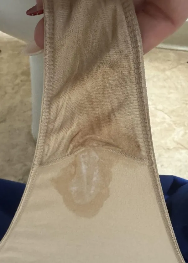 ベージュのパンティの股間部分に白濁したマン汁がべっとり付着している様子を写した画像で、女の股間の濃厚なオリモノの痕跡がはっきりと確認できる一枚。