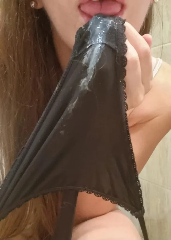 黒いパンティの股間に白濁したマン汁とオリモノがべっとり付着し、それを女が舌で舐めている様子を捉えた一枚