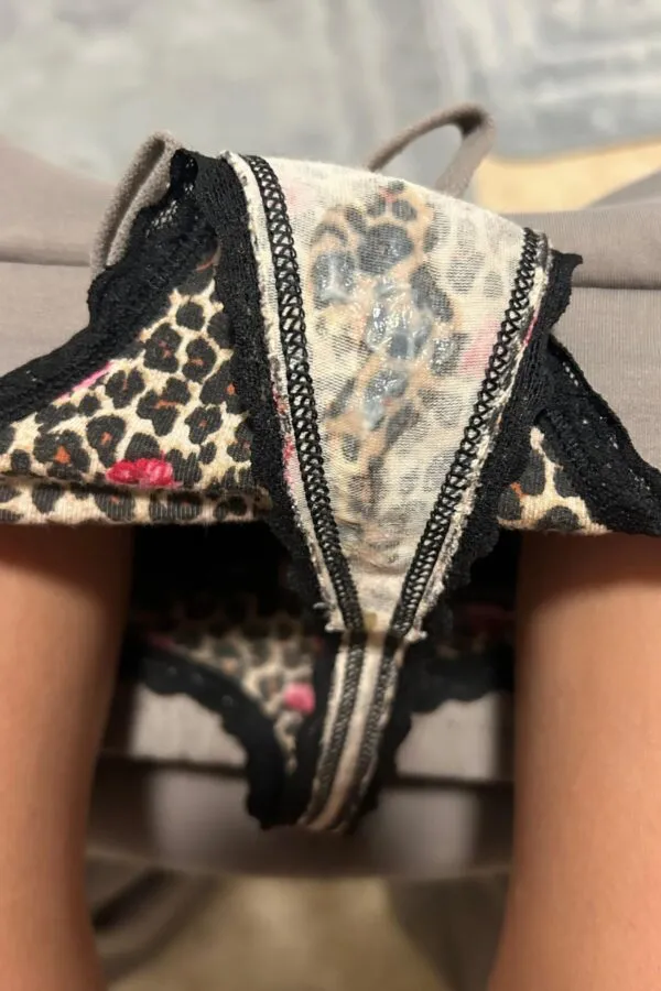 女性が座った状態でヒョウ柄のパンティをずらしてクロッチ部分に白濁したマン汁とオリモノ濃厚にべっとり付着しているのを見せる写真。