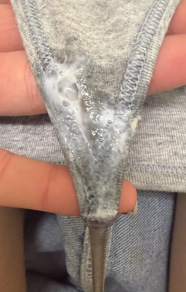 グレーのTバックパンティ股間にべっとり付着した白濁したマン汁が濃厚に絡みついているのを手で広げて見せている様子