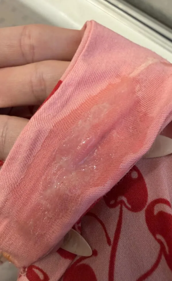 ピンク色のパンティの股間部分に白濁したマン汁がべっとり付着している様子を捉えた一枚で、女性の淫らなオリモノの濃厚な質感がリアルに伝わる画像。