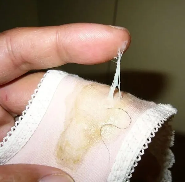 女の股間に密着した薄ピンク色のパンティにマン汁がべっとり付着し、指で引き伸ばされるクリーミーに濡れたオリモノの様子が映し出された淫らなエロ画像。