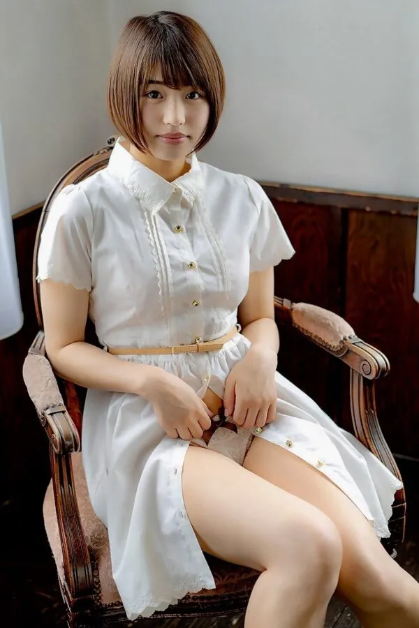 白いワンピースを着た女が椅子に座り、自らスカートをめくってベージュのパンティを見せる淫らな股間を撮影したエロ画像