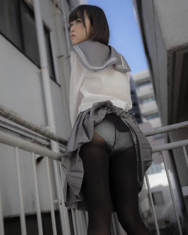 パンストを履いたグレーのスカートをたくし上げ、屋外の狭い通路で振り返るJKの尻を撮影した卑猥なエロ画像