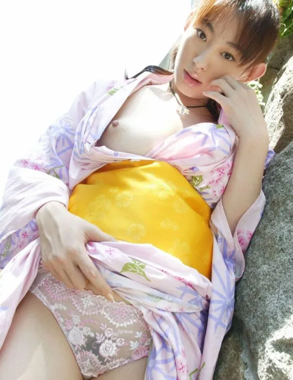 野外で薄紫の花柄の着物をめくり上げ、ピンクと白のレース模様のパンティを露出させて座る女の淫らな股間を撮影したエロ画像